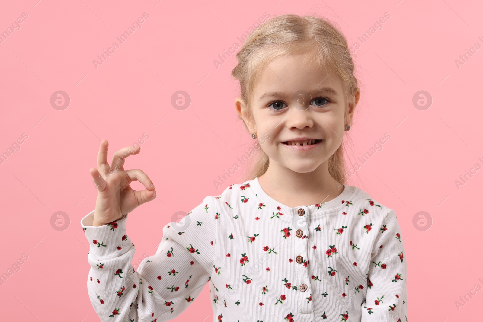 Photo of Cute little girl showing OK gesture on pink background