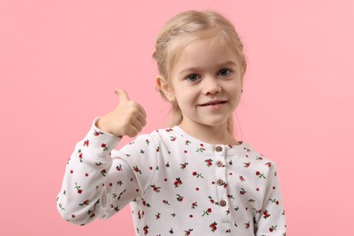 Photo of Cute little girl showing thumbs up on pink background