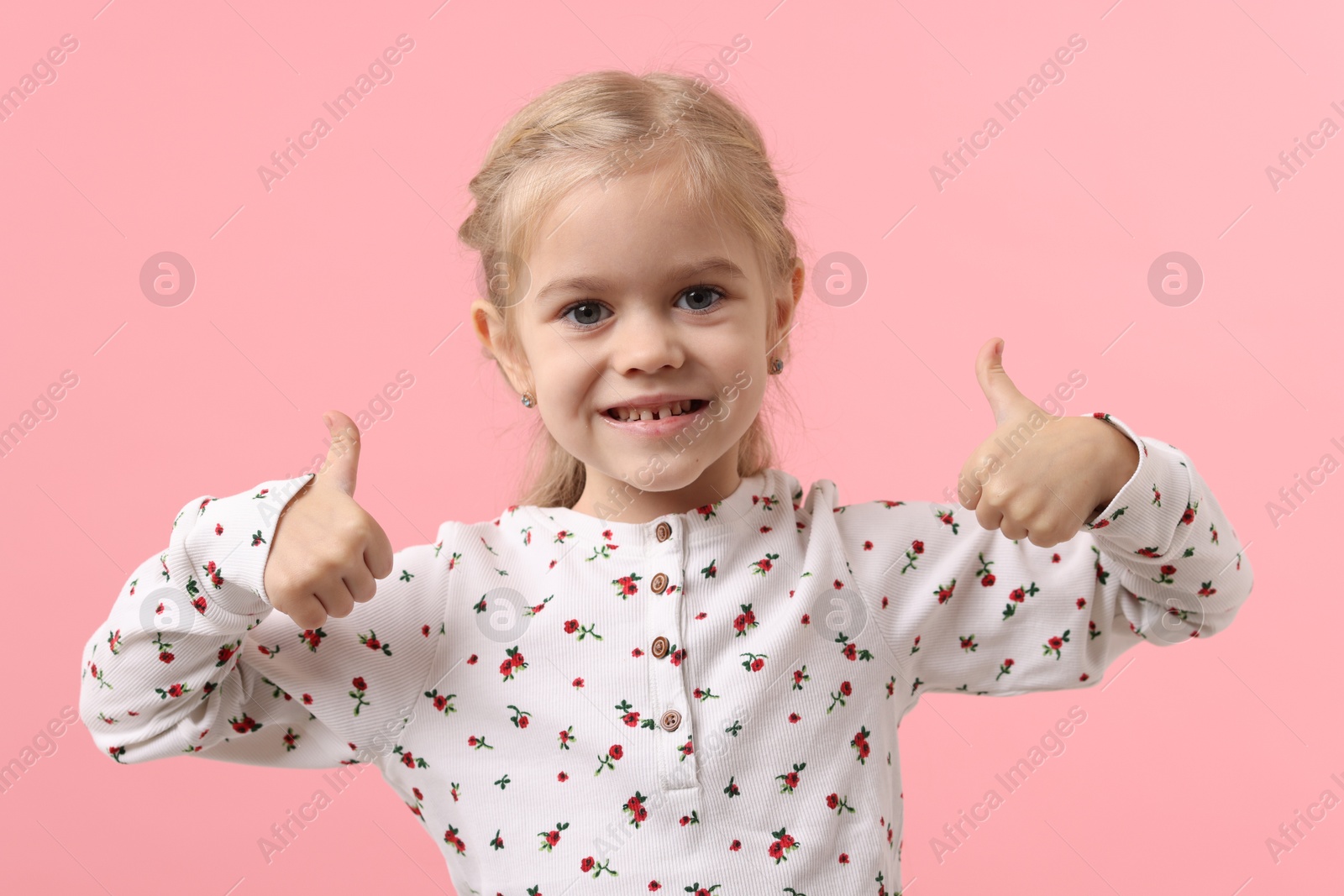 Photo of Cute little girl showing thumbs up on pink background