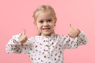 Photo of Cute little girl showing thumbs up on pink background