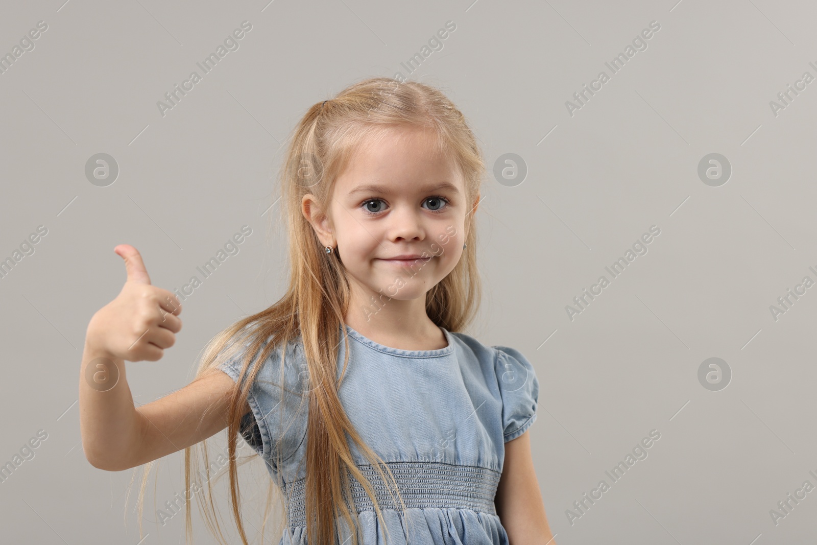 Photo of Cute little girl showing thumbs up on gray background, space for text