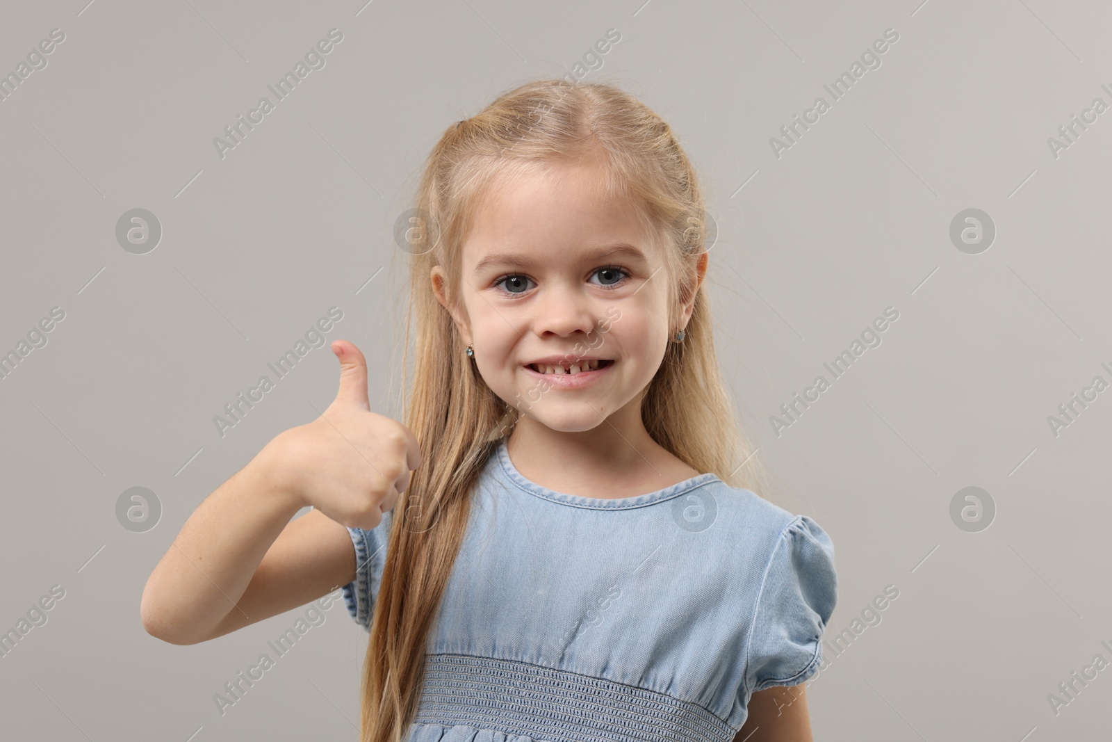 Photo of Cute little girl showing thumbs up on gray background