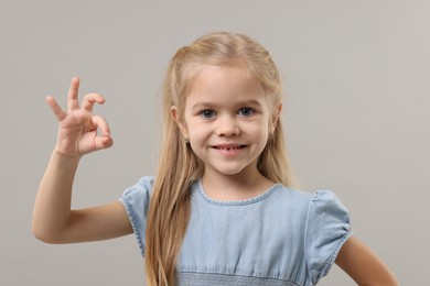 Photo of Cute little girl showing OK gesture on gray background