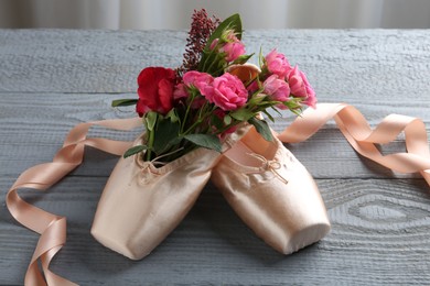 Photo of Pair of beautiful pointe shoes and flowers on grey wooden table