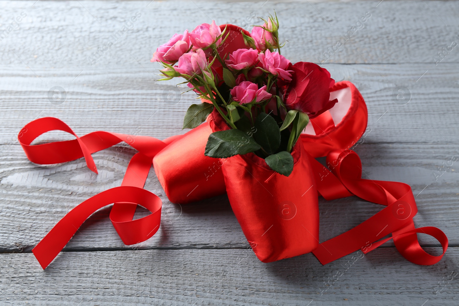 Photo of Pair of red pointe shoes and flowers on grey wooden table