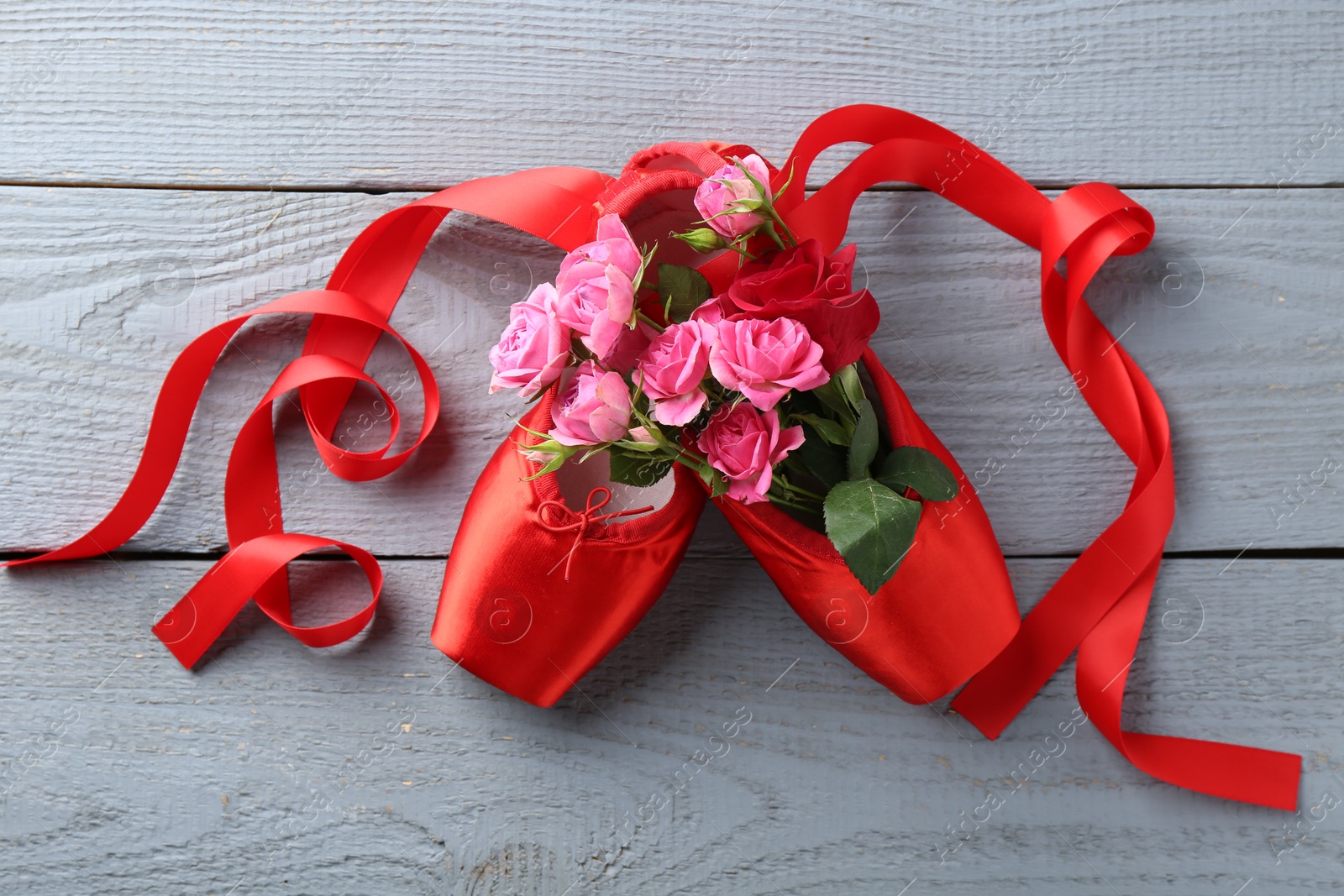 Photo of Pair of red pointe shoes and flowers on grey wooden table, top view