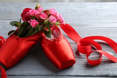 Photo of Pair of red pointe shoes and flowers on grey wooden table