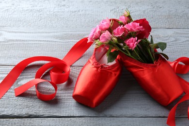 Photo of Pair of red pointe shoes and flowers on grey wooden table