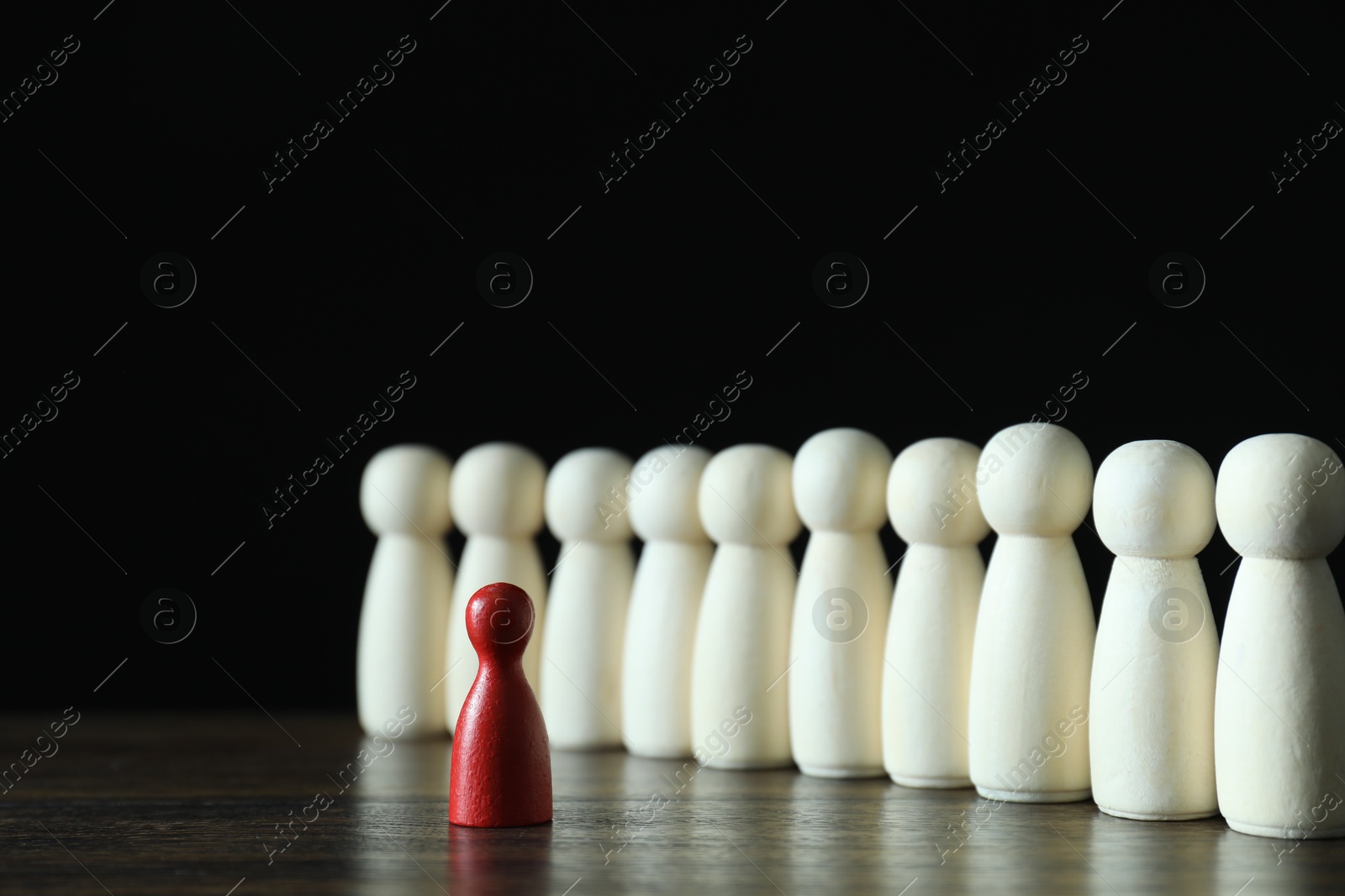 Photo of Human resources concept. Red figure in front of wooden ones on table against dark background, closeup. Space for text