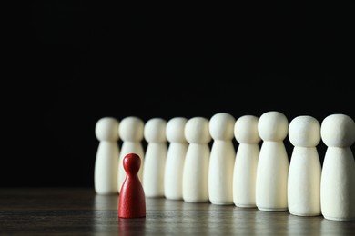 Photo of Human resources concept. Red figure in front of wooden ones on table against dark background, closeup. Space for text