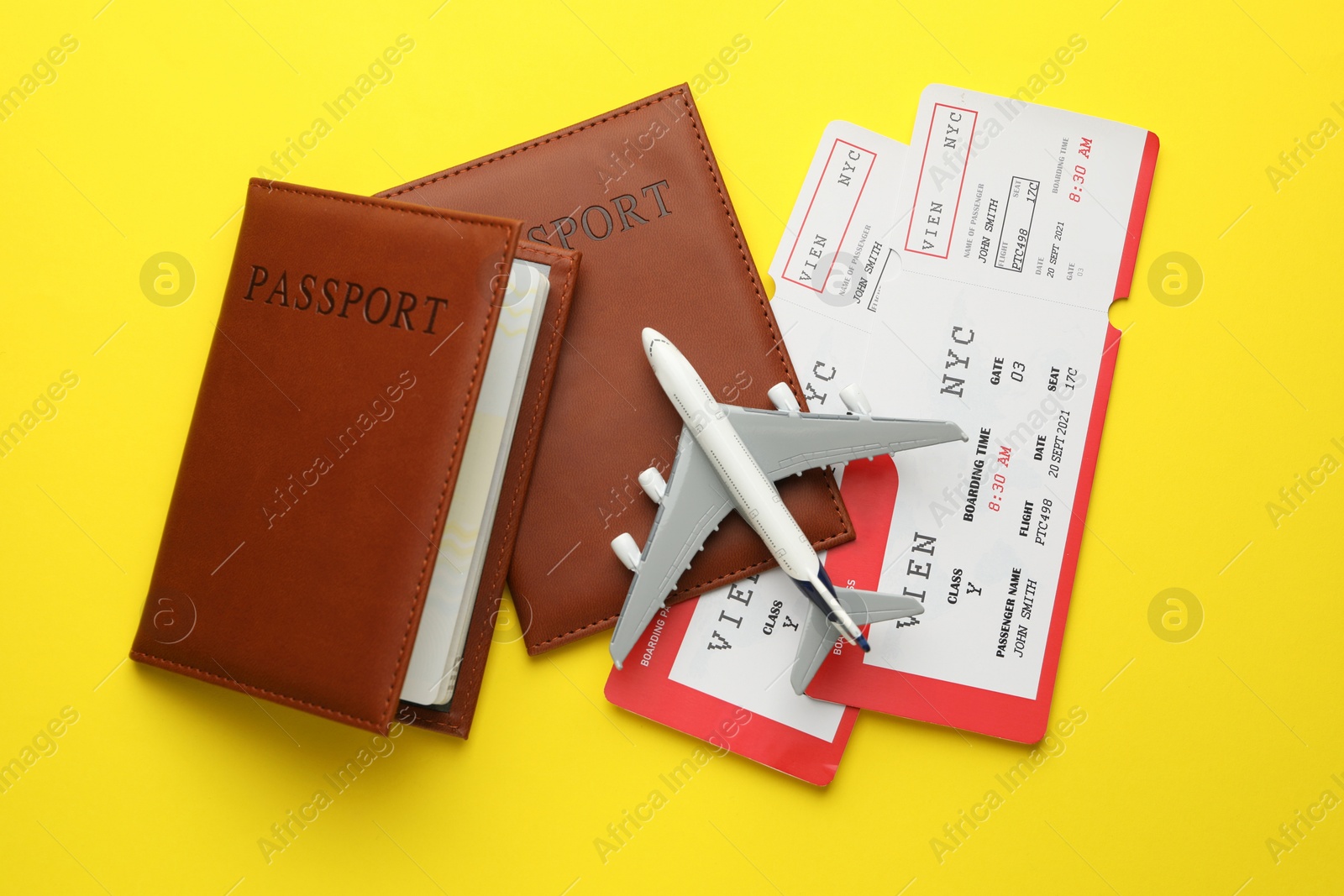 Photo of Travel agency. Flight tickets, passports and plane model on yellow background, flat lay