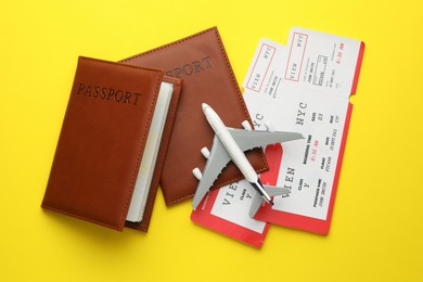 Photo of Travel agency. Flight tickets, passports and plane model on yellow background, flat lay