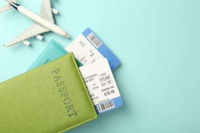 Passport with tickets and plane model on light blue background, top view. Space for text