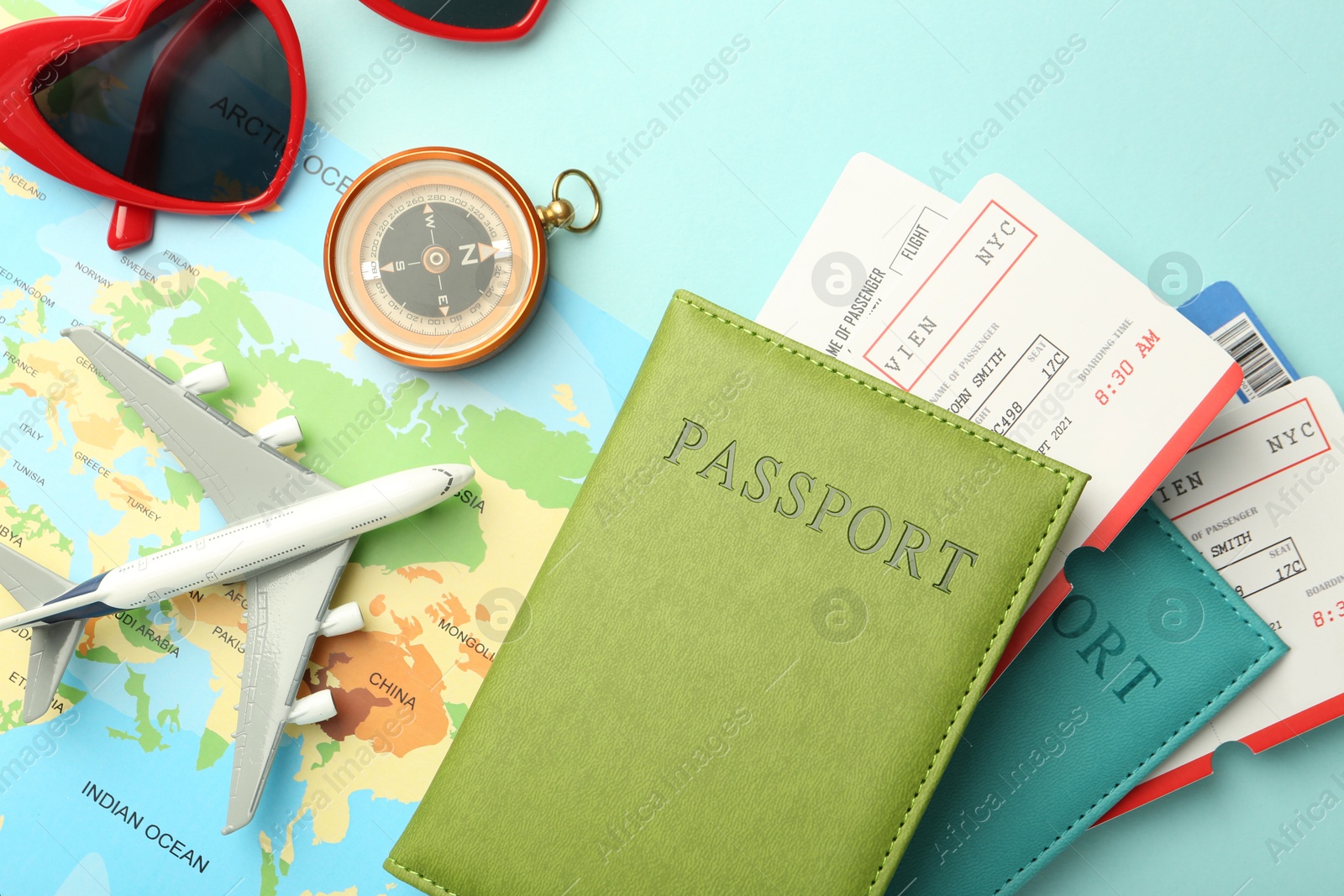 Photo of Passports with tickets, map, compass, plane model and sunglasses on light blue background, flat lay