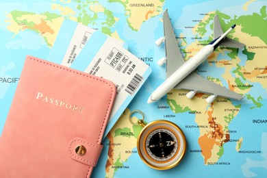 Photo of Passport with tickets, compass and plane model on world map, flat lay