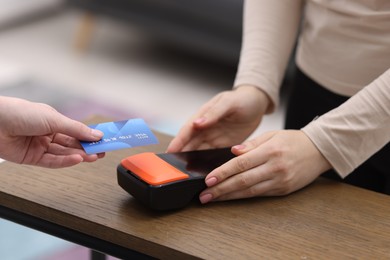 Photo of Woman paying with credit card via terminal at wooden counter indoors, closeup