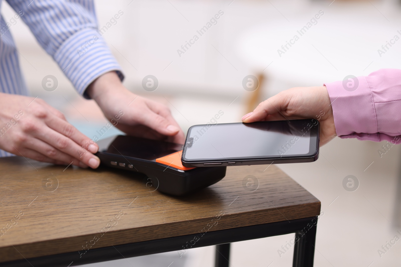 Photo of Woman paying with smartphone via terminal at wooden counter indoors, closeup