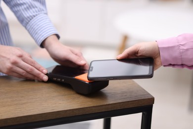 Photo of Woman paying with smartphone via terminal at wooden counter indoors, closeup