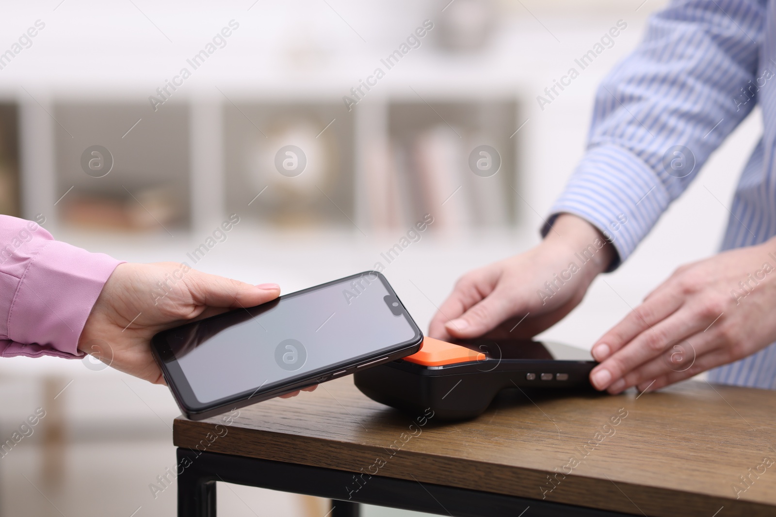 Photo of Woman paying with smartphone via terminal at wooden counter indoors, closeup