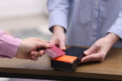 Photo of Woman paying with credit card via terminal at wooden counter indoors, closeup