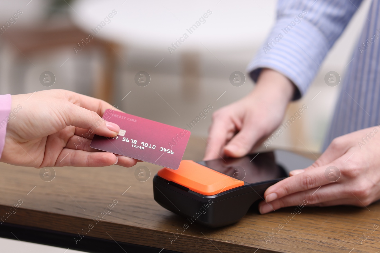 Photo of Woman paying with credit card via terminal at wooden counter indoors, closeup