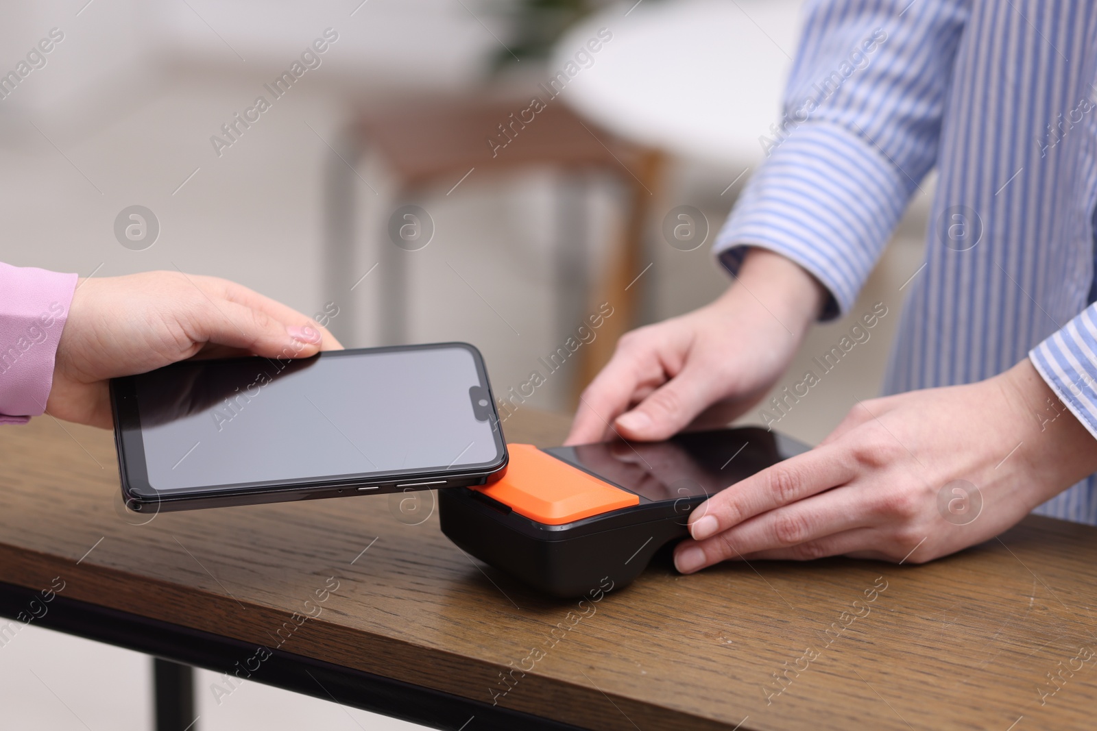 Photo of Woman paying with smartphone via terminal at wooden counter indoors, closeup