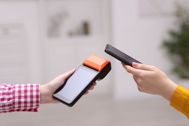 Photo of Woman paying with smartphone via terminal against blurred background, closeup