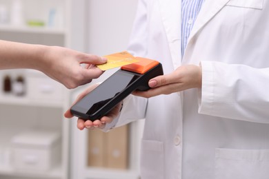 Photo of Woman paying with credit card via terminal against blurred background, closeup