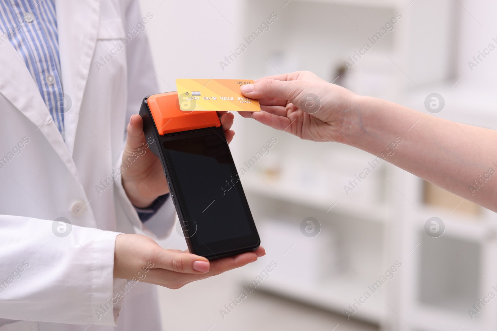 Photo of Woman paying with credit card via terminal against blurred background, closeup