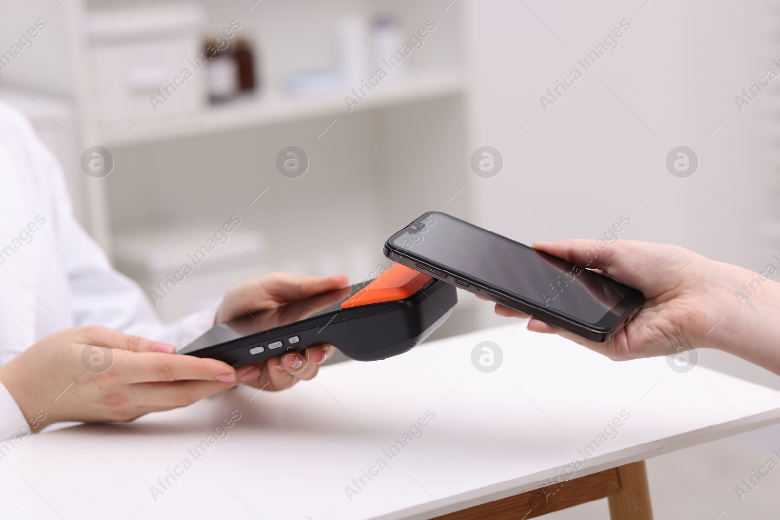 Photo of Woman paying with smartphone via terminal at counter indoors, closeup