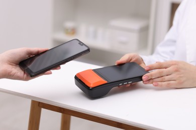 Photo of Woman paying with smartphone via terminal at counter indoors, closeup