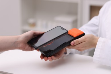 Photo of Woman paying with smartphone via terminal at counter indoors, closeup