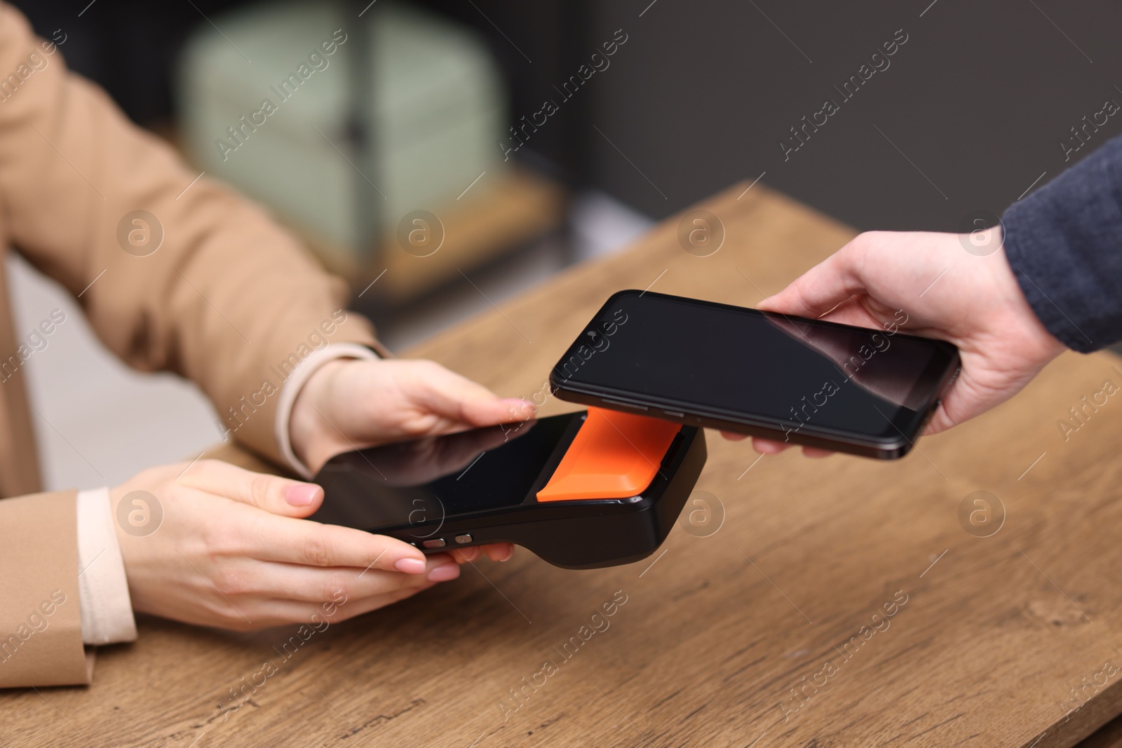 Photo of Woman paying with smartphone via terminal at wooden counter indoors, closeup