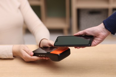 Photo of Woman paying with smartphone via terminal at wooden counter indoors, closeup