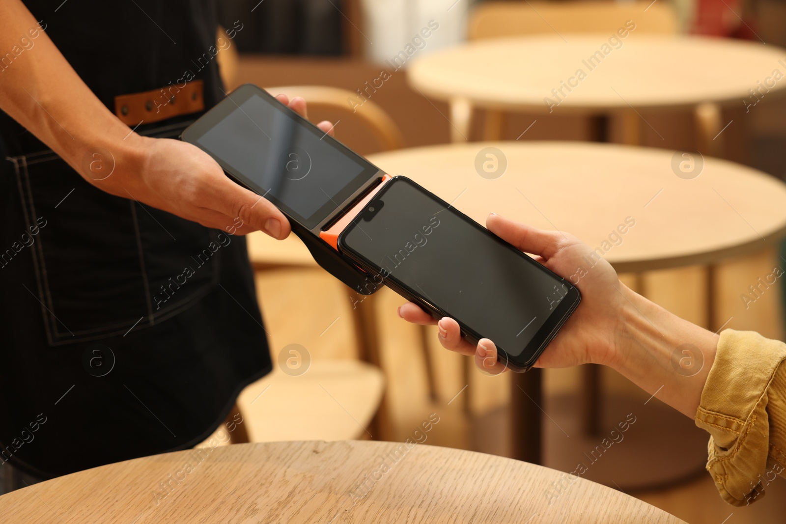 Photo of Woman paying with smartphone via terminal at wooden table in cafe, closeup