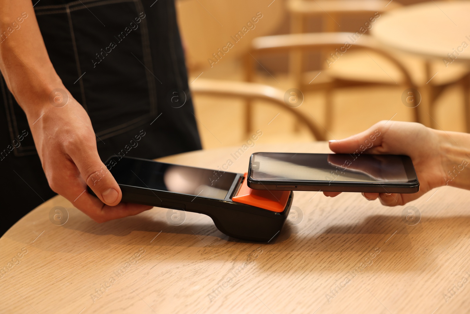 Photo of Woman paying with smartphone via terminal at wooden table in cafe, closeup