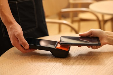 Photo of Woman paying with smartphone via terminal at wooden table in cafe, closeup