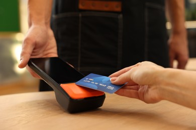 Photo of Woman paying with credit card via terminal at wooden table in cafe, closeup