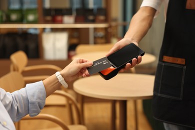 Photo of Woman paying with credit card via terminal at wooden table in cafe, closeup