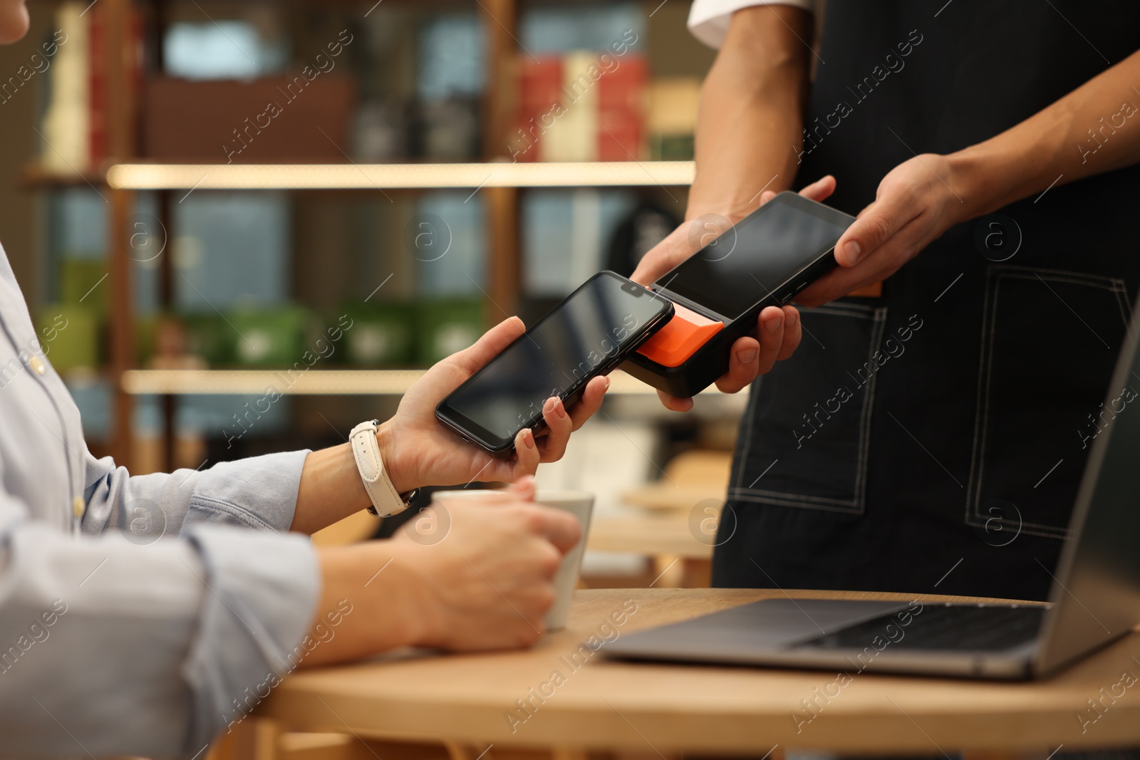 Photo of Woman paying with smartphone via terminal at wooden table in cafe, closeup