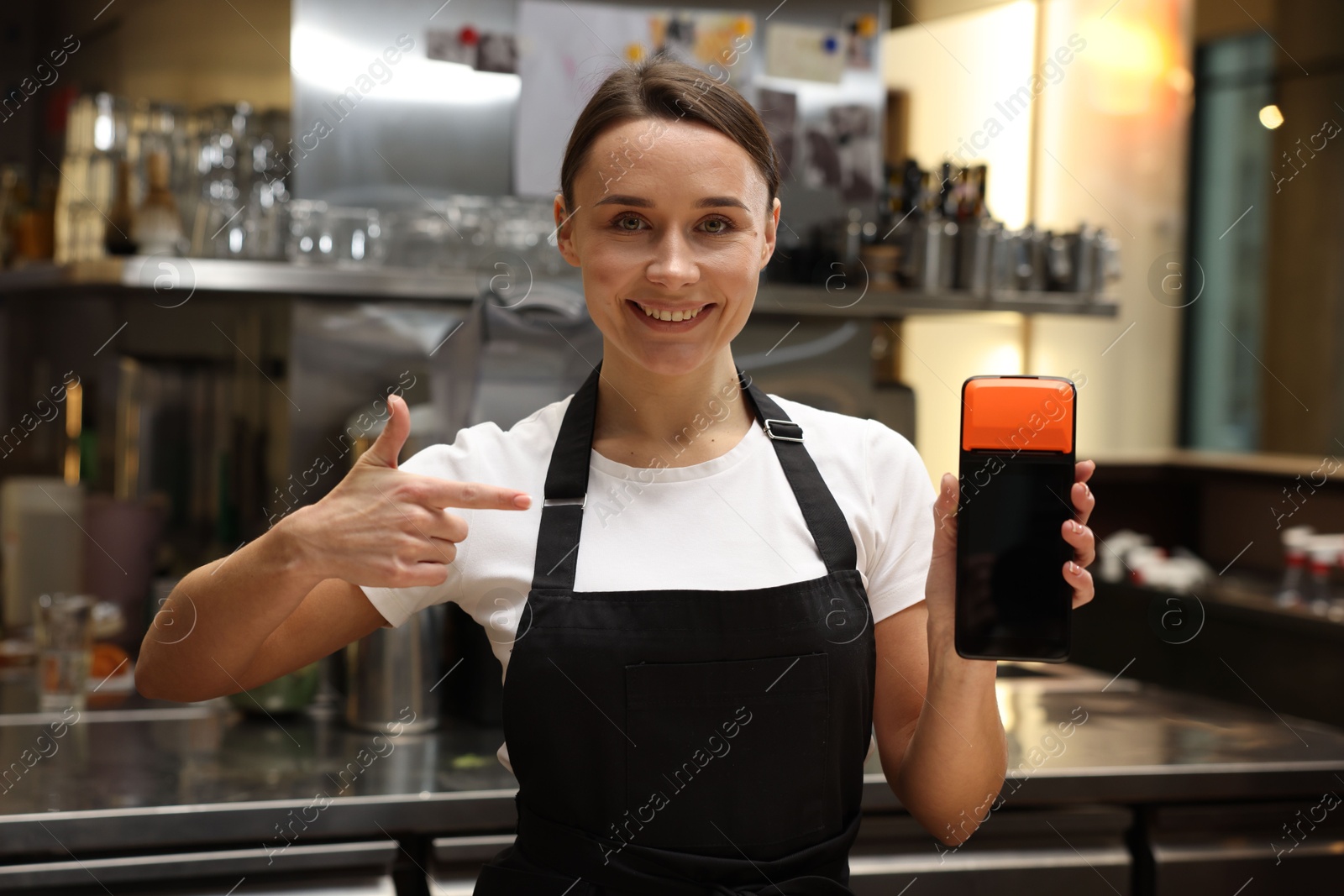 Photo of Smiling cafe worker pointing at payment terminal indoors