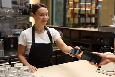 Photo of Cafe worker taking payment from client via terminal indoors