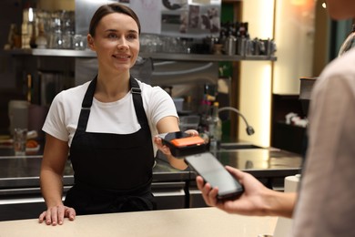 Photo of Cafe worker taking payment from client via terminal indoors