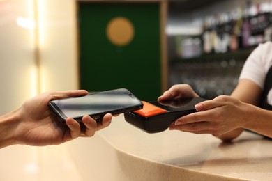 Photo of Man paying with smartphone via terminal in cafe, closeup