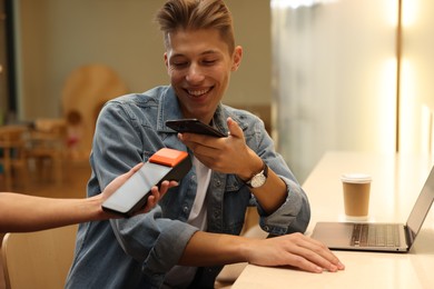 Photo of Man paying with smartphone via terminal in cafe