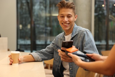 Photo of Man paying with smartphone via terminal in cafe