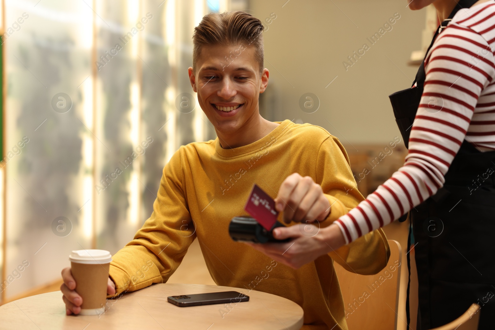 Photo of Man paying with credit card via terminal at wooden table in cafe