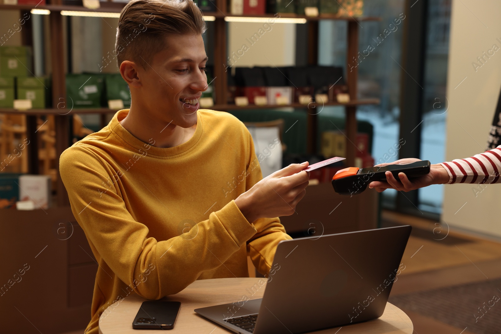 Photo of Man paying with credit card via terminal at wooden table in cafe