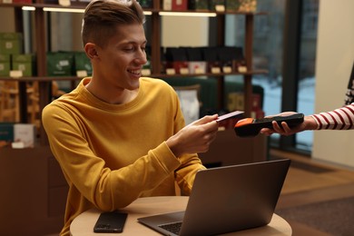 Photo of Man paying with credit card via terminal at wooden table in cafe