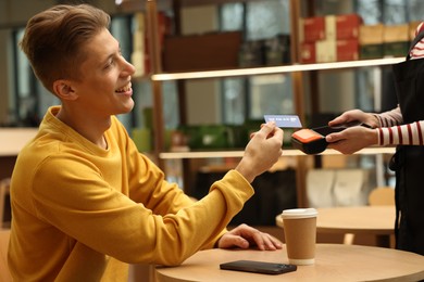 Photo of Man paying with credit card via terminal at wooden table in cafe